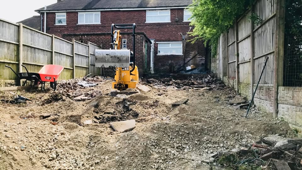 Cheddleton garden during digger groundworks between timber boundary fences, with soil and rubble cleared